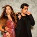 Um casal de atores turcos posando para foto: a mulher à esquerda usa um vestido floral escuro e o homem à direita veste um terno preto com camiseta preta. No centro, uma faixa amarela e preta contém o texto "5 COISAS PROIBIDO NAS NOVELAS TURCAS".