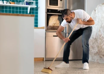 Homem varrendo a casa na cozinha com uma vassoura, em um momento de limpeza doméstica.