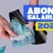 Mãos colocando notas de cem reais em carteira preta ao lado de texto sobre abono salarial 2026.