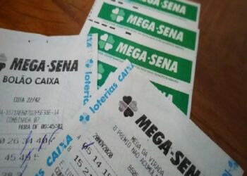 Bilhetes de bolão da Mega-Sena sobre mesa de madeira, com apostas agrupadas