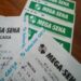Bilhetes de bolão da Mega-Sena sobre mesa de madeira, com apostas agrupadas