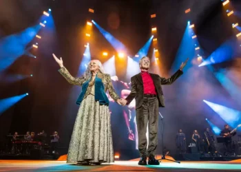 Caetano Veloso e Maria Bethânia conquistam o Grammy 2026 na categoria música global 5 Dois artistas brasileiros se apresentam juntos em um palco iluminado, de mãos dadas, durante um espetáculo musical com banda ao fundo.