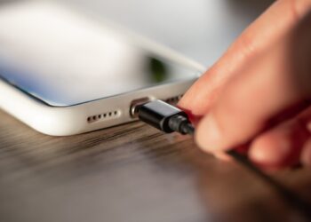 Mão conectando cabo de carregador em smartphone branco sobre mesa de madeira