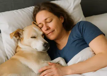 Mulher deitada na cama abraçando um cachorro.