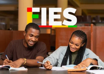 Dois estudantes escrevem e sorriem em ambiente de estudos, com livros e logo do FIES ao fundo.