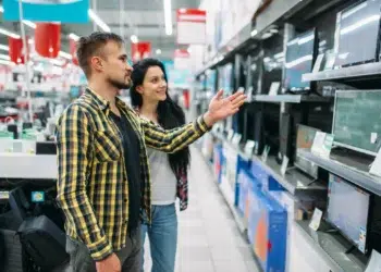 Casal observando diferentes modelos de monitores em uma loja de eletrônicos antes da compra.