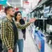 Casal observando diferentes modelos de monitores em uma loja de eletrônicos antes da compra.