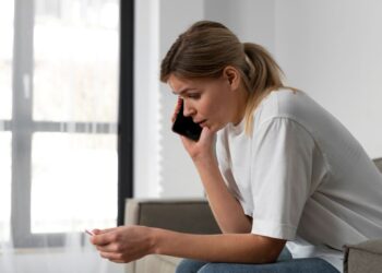Mulher preocupada e conversando ao telefone, em um ambiente doméstico, representando a importância de denunciar casos de violência contra a mulher.