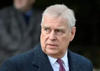 Homem de expressão séria usando terno escuro e gravata vermelha em ambiente externo