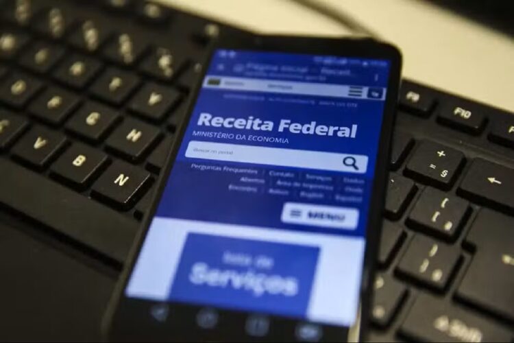 Quem ganha até R$ 5 mil receberá alerta da Receita no WhatsApp sobre isenção do IR 1 Celular com site da Receita Federal exibido sobre teclado preto de computador