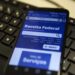 Celular com site da Receita Federal exibido sobre teclado preto de computador