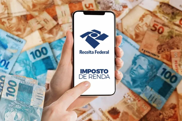 Receita Federal paga lote da malha fina do Imposto de Renda de fevereiro; veja se você está na lista 1 Mãos segurando celular com tela da Receita Federal e notas de real ao fundo.