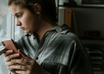 Adolescente olhando para o celular enquanto reflete sobre o ghosting, um fenômeno moderno de abandono emocional, onde a comunicação é abruptamente interrompida sem explicações.