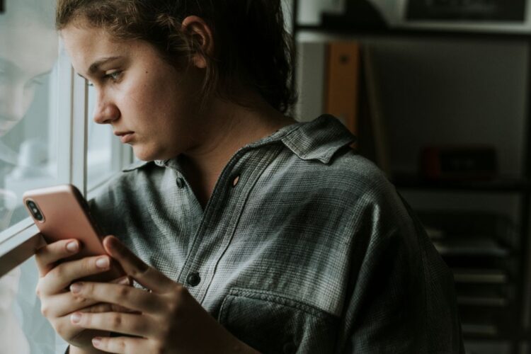 Adolescente olhando para o celular enquanto reflete sobre o ghosting, um fenômeno moderno de abandono emocional, onde a comunicação é abruptamente interrompida sem explicações.