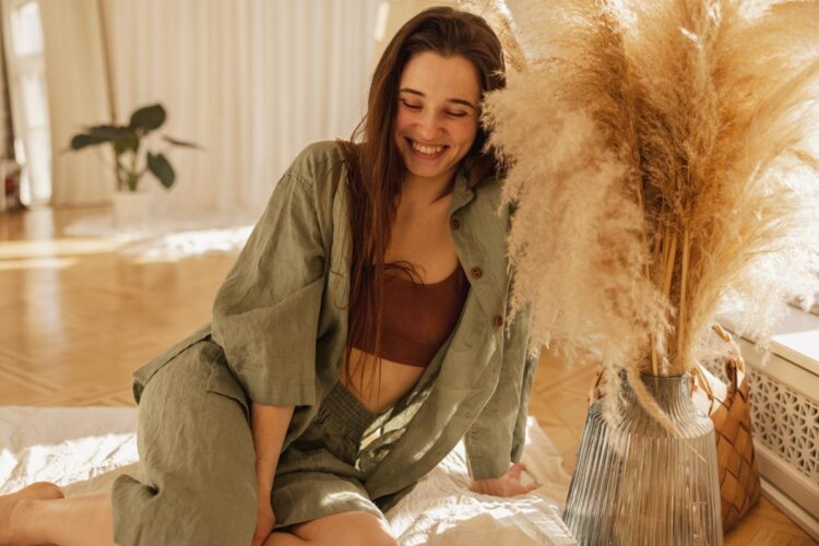 O que as suas "roupas de ficar em casa" dizem sobre você? A ciência revela o impacto silencioso na sua autoestima 1 Mulher sorridente usando conjunto de linho verde em ambiente acolhedor com decoração natural