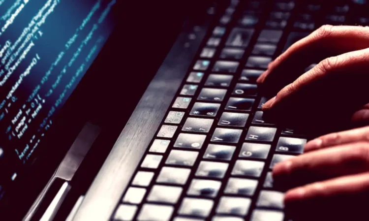 Alerta de segurança: Se você tem este aplicativo instalado, seu banco pode estar em risco 1 Mãos de pessoa digitando rapidamente em teclado de notebook com tela exibindo linhas de código, exemplificando ataques e golpes, através de aplicativos falsos