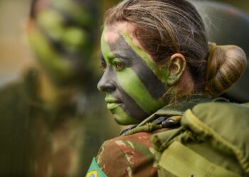 Militar brasileira com pintura camuflada no rosto durante atividade de instrução, representando a seleção feminina para o serviço militar.