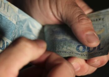 Mãos segurando e contando notas de cem reais do Bolsa Família