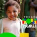 Menina negra sorridente em primeiro plano, vestindo casaco claro, com o logotipo colorido do Programa Bolsa Família sobreposto à direita. Ao fundo, uma figura adulta desfocada em um ambiente externo ensolarado. A imagem transmite o impacto social do benefício na infância.