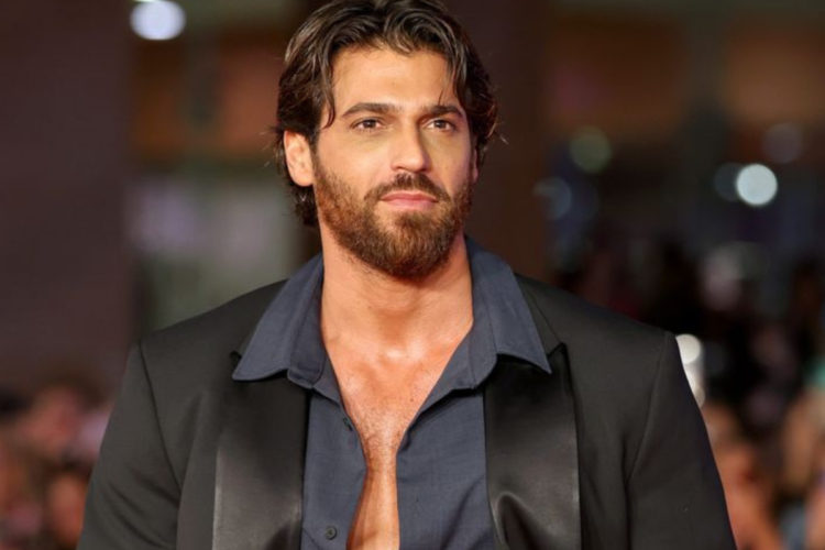 Homem de barba e cabelo castanho veste terno preto e camisa azul em ambiente sofisticado