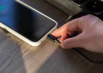 Celular sendo carregado com capinha enquanto o cabo é conectado, ilustrando risco de aquecimento da bateria.