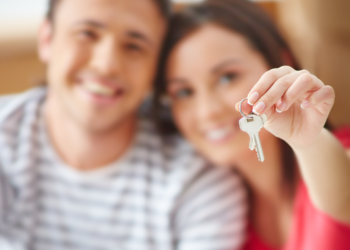 Casal sorridente segura chaves de imóvel com fundo desfocado