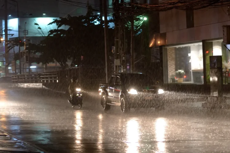 Última semana do mês terá temporais e chuva generalizada; confira a previsão completa 1 Carros e motocicleta trafegam sob chuva forte à noite em avenida urbana durante temporal.