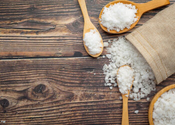Sal grosso em colheres de madeira e saco de juta sobre superfície rústica representando o problema do sal úmido na cozinha