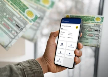 Mão masculina segurando um smartphone que exibe o aplicativo oficial "Carteira Digital de Trânsito" com dados de condutor, tendo ao fundo versões impressas da Nova CNH verde e amarela desfocadas.