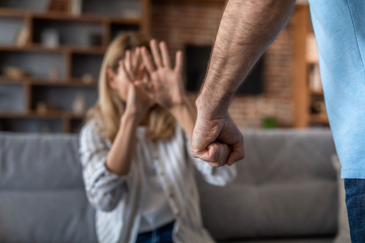 Ligue 180 pode virar alerta obrigatório em notícias de violência contra a mulher; saiba mais 2 Mulher se protegendo de um homem agressivo, em um ambiente doméstico, ilustrando uma situação de violência doméstica.