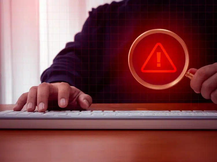 Falsos empregos no Sudeste Asiático! Itamaraty avisa brasileiros para ficarem atentos 1 Mão digitando em teclado com lupa exibindo símbolo de alerta vermelho