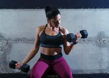 Mulher levantando halteres na academia, simbolizando o estudo sobre a relação entre postagens de treino e narcisismo.