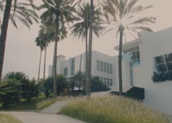 Mansão branca de dois andares cercada por palmeiras e jardim bem cuidado