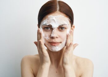 Mulher espalha máscara cremosa de pó de arroz no rosto usando as mãos frente a fundo claro