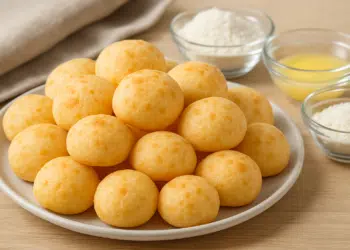 Prato com pães de queijo e ingredientes ao fundo