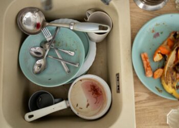 Louça suja em pia, com pratos, talheres e xícaras, simbolizando o comportamento excessivo de limpeza.