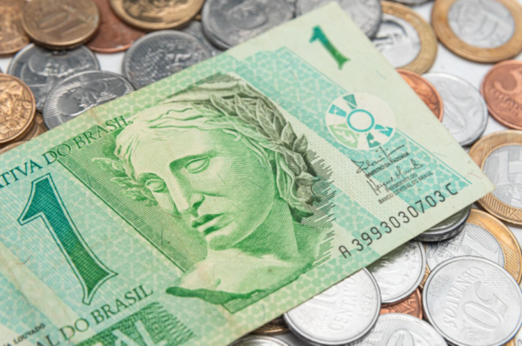 4 simpatias poderosas para atrair mais dinheiro neste mês de março 1 Close-up de uma cédula de um real verde e diversas moedas de Real de diferentes valores espalhadas sobre uma superfície branca. O foco principal está na efígie da República na nota, simbolizando a circulação de dinheiro e a riqueza.