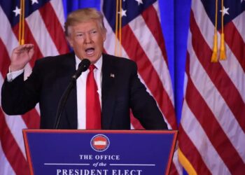 O Presidente Donald Trump em um púlpito com o selo presidencial, falando ao microfone com várias bandeiras dos Estados Unidos ao fundo.