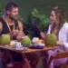Participantes Jonas e Ana Paula sentados à mesa com drinks de coco durante conversa em clima de tensão e flerte durante festa no BBB 26
