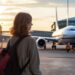Passageira com mochila observa avião no aeroporto, representando cancelamento de voos do Brasil para a Argentina devido à greve.
