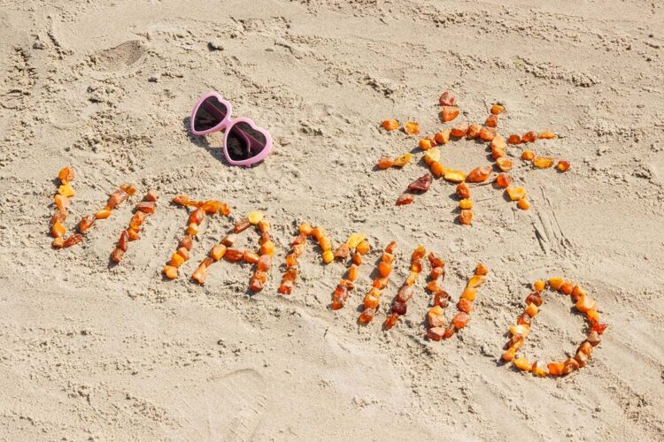 Vitamina D baixa? O sintoma silencioso que aparece nas unhas e quase ninguém observa 1 Palavra “Vitamina D” escrita na areia da praia com pequenas pedras alaranjadas, ao lado de um desenho de sol e óculos de sol em formato de coração.