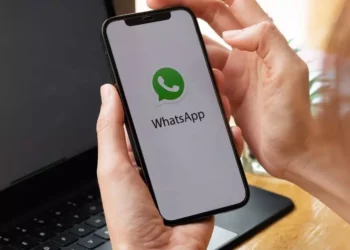 Pessoa segurando celular com WhatsApp aberto em frente a notebook