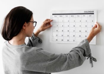 Mulher de óculos coloca calendário na parede e observa as datas com atenção