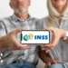 Casal idoso segura celular exibindo logotipo do INSS na tela, focado nas mãos
