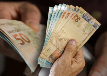 Homem segurando notas de R$ 50,00 e R$ 100,00.