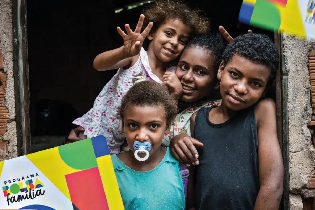 Calendário Bolsa Família de abril traz novidades para mais de 18 milhões de famílias 2 Quatro crianças próximas sorrindo e abraçadas em janela simples com cartão do Bolsa Família visível