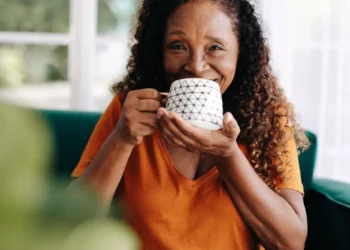 Mulher sênior sorri segurando xícara de café branca com estampa geométrica