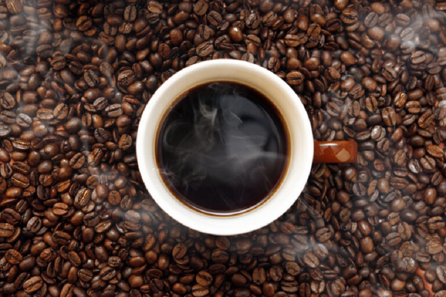 Café diário pode trazer benefícios para um envelhecimento mais saudável; entenda! 2 Xícara de café preto soltando vapor sobre camada de grãos torrados