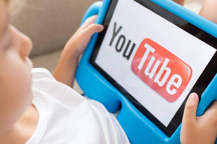 Assistir a outras crianças abrindo brinquedos pode gerar um sentimento negativo no seu filho 1 Criança segurando tablet com logo do YouTube exibido na tela enquanto assiste vídeos
