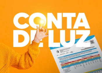 Pessoa com suéter laranja segura lâmpada acesa ao lado de conta de luz em fundo amarelo.